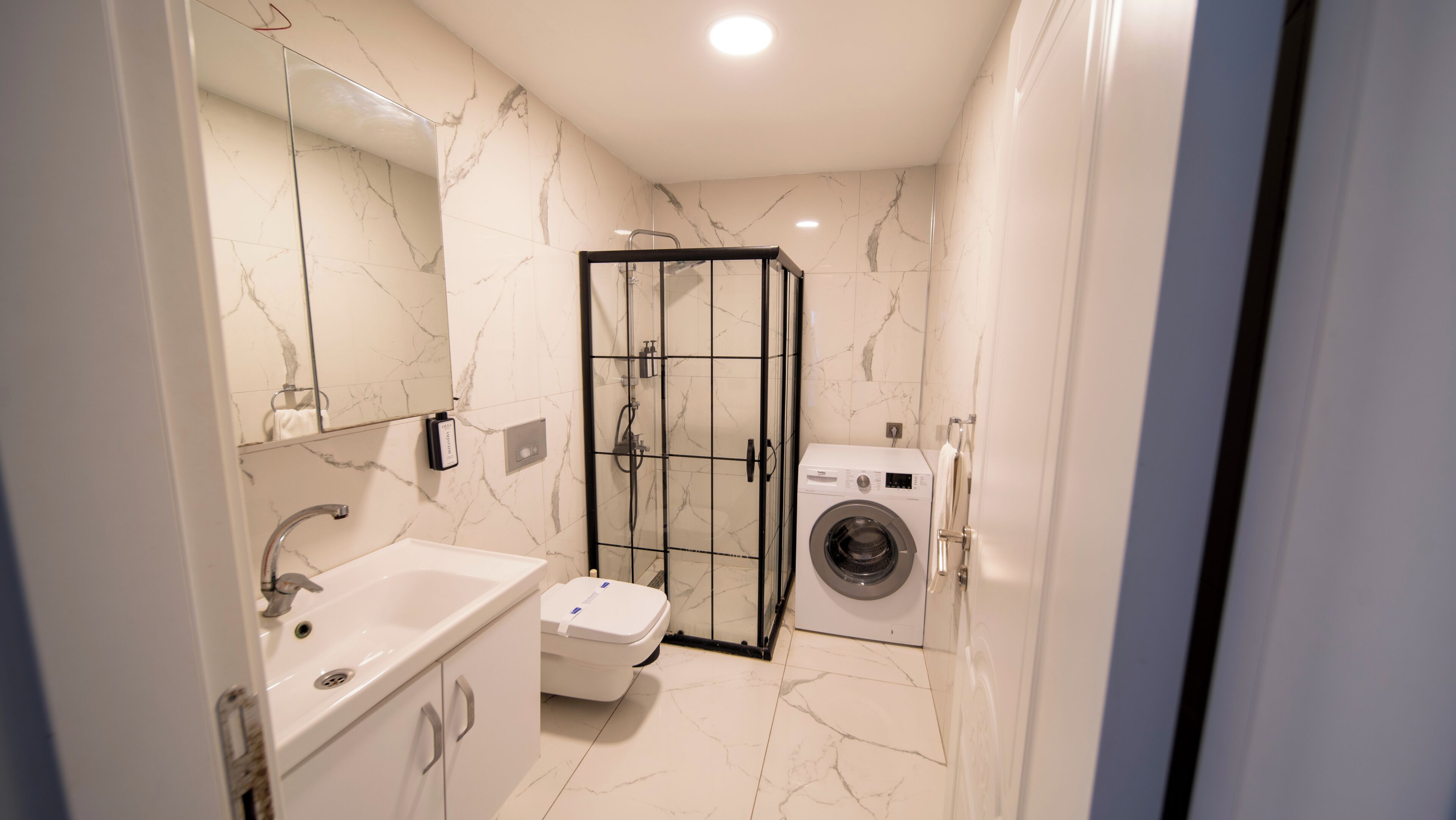 Un bagno moderno con box doccia in vetro, lavatrice a incasso e mobile lavabo.