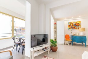 Ein modernes Wohnzimmer mit Flachbildfernseher, Topfpflanze, blauer Kommode und einem farbenfrohen, abstrakten Gemälde.