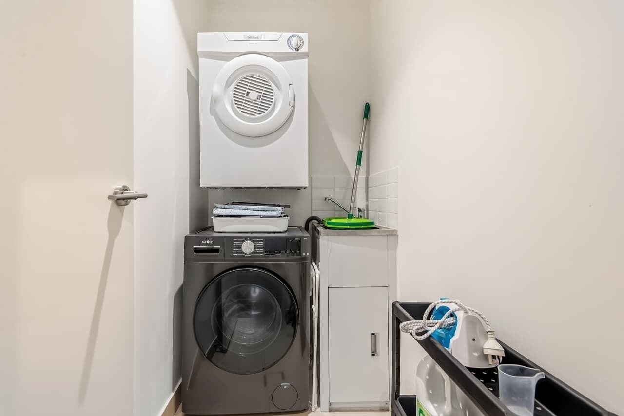Uma área de lavanderia compacta com máquina de lavar, secadora e um esfregão.