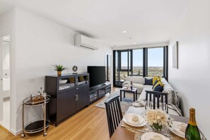 Ein modernes Wohnzimmer mit Essbereich, einer schwarzen Unterhaltungsecke und einem großen Fenster mit Blick auf die Stadt.