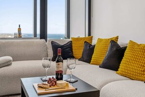 Ein modernes Wohnzimmer mit einer Couch, einem Couchtisch mit Snacks und Wein und Blick auf den Ozean.