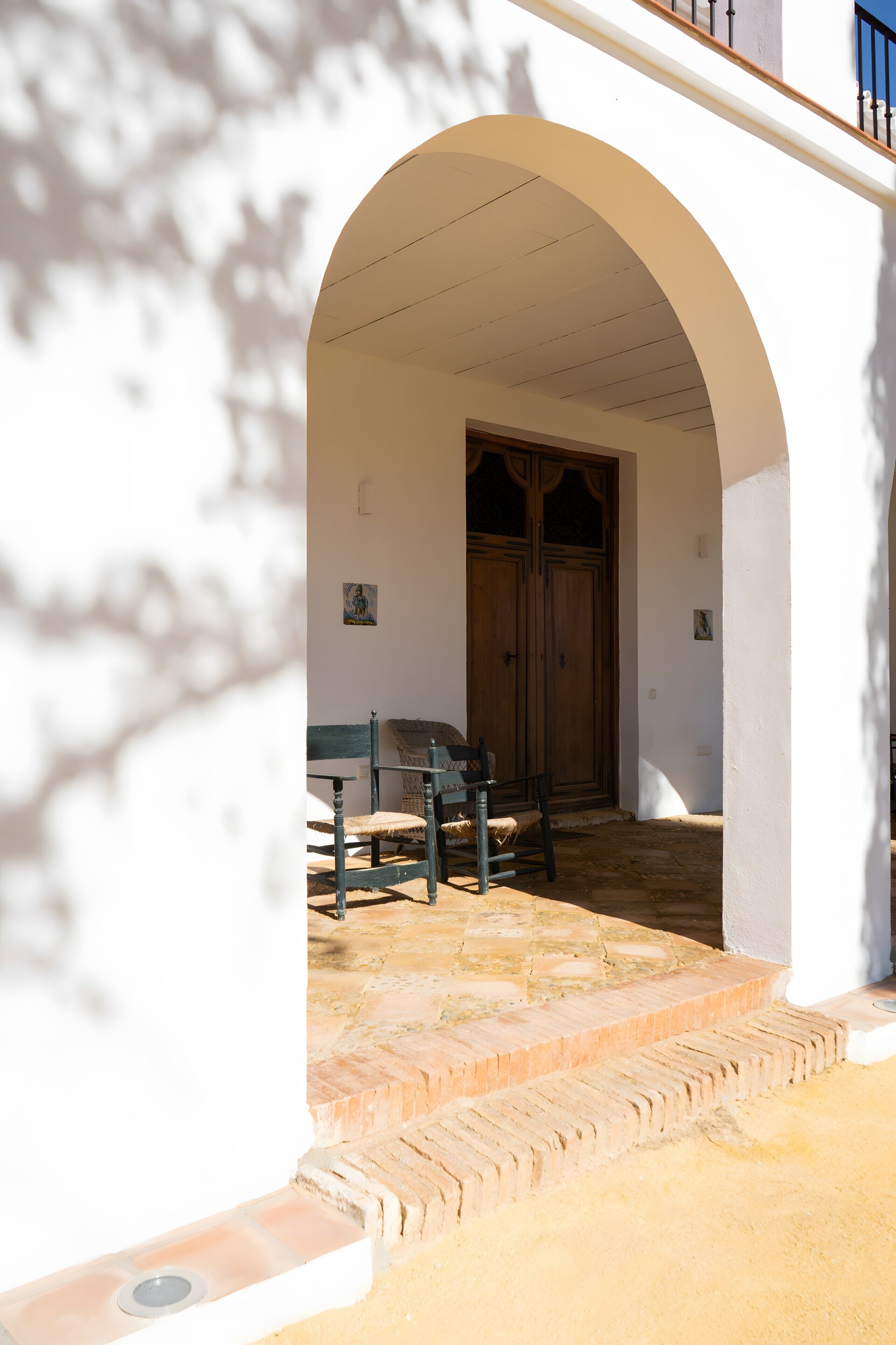 An arched doorway leading to a room with a wooden door, a bench, and a small table.