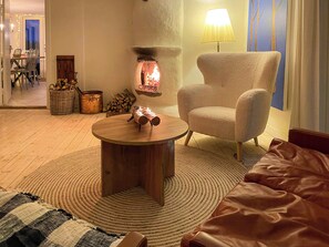Ein gemütliches Wohnzimmer mit Kamin, einem runden Holztisch, einem bequemen Sessel und einer Couch.