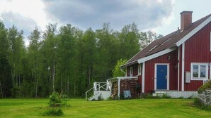 En rød lade med en blå dør, et bålsted med brænde, og en græsplæne.