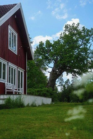 Ein rotes Gebäude mit einer weißen Veranda und einem großen Baum davor.