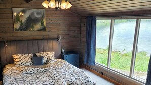 Une chambre avec un grand lit, une vue sur un lac, un plafond en bois et un tableau au mur.