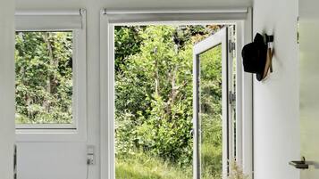 Une chambre à coucher comprenant un lit, un banc en bois, un vase avec une plante et une porte-fenêtre coulissante donnant sur une terrasse extérieure.