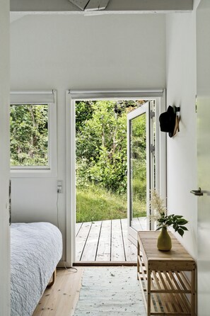 Et soveværelse med en seng, en træbænk, en vase med en plante og en skydedør, der fører til en terrasse.