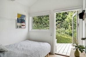 A bedroom with a bed, a window, and a view of greenery outside. - Sunset over Sejerø Bay from house (Fårevejle)
