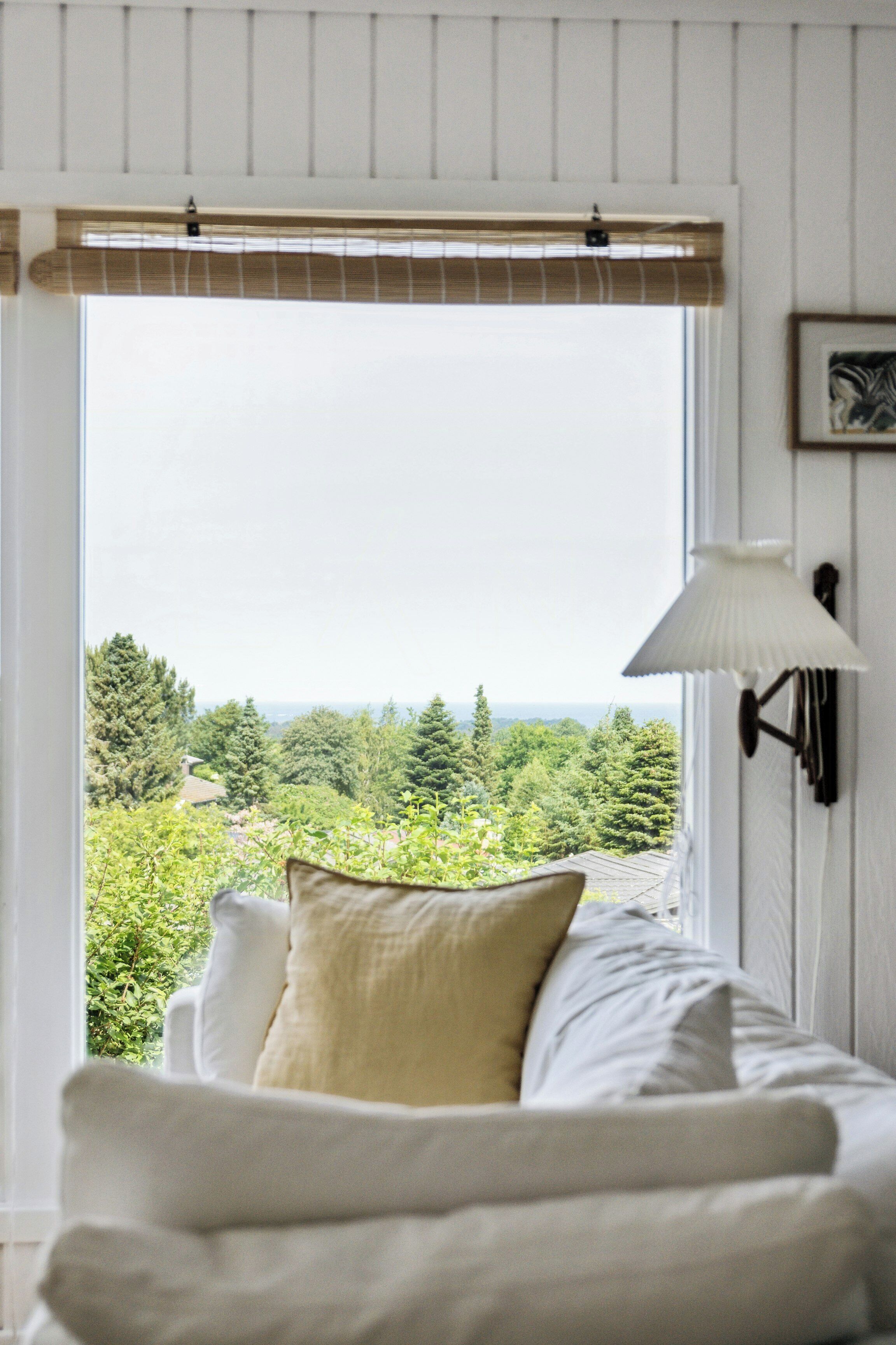 Une chambre avec un lit, une fenêtre donnant sur un paysage verdoyant et une lampe fixée au mur.
