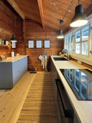 A wooden interior with a kitchen area, wooden ceiling beams, and framed pictures on the wall. - Authentic log cabin on large enclosed natural plot (Vig)