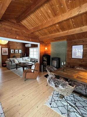 A cozy cabin interior with a wooden ceiling, a fireplace, a dining table, and a sofa. - Authentic log cabin on large enclosed natural plot (Vig)