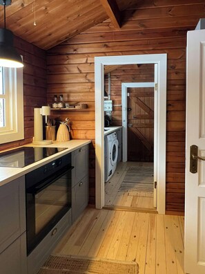 A kitchen with wooden walls, a washing machine, and a stove. - Authentic log cabin on large enclosed natural plot (Vig)