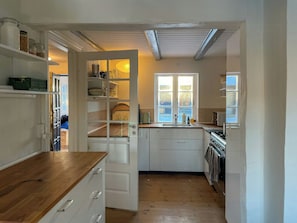 Eine Küche mit weißen Schränken, einer Holzausziehtheke, einem Fenster mit Blick und einer Tür zu einem anderen Raum.