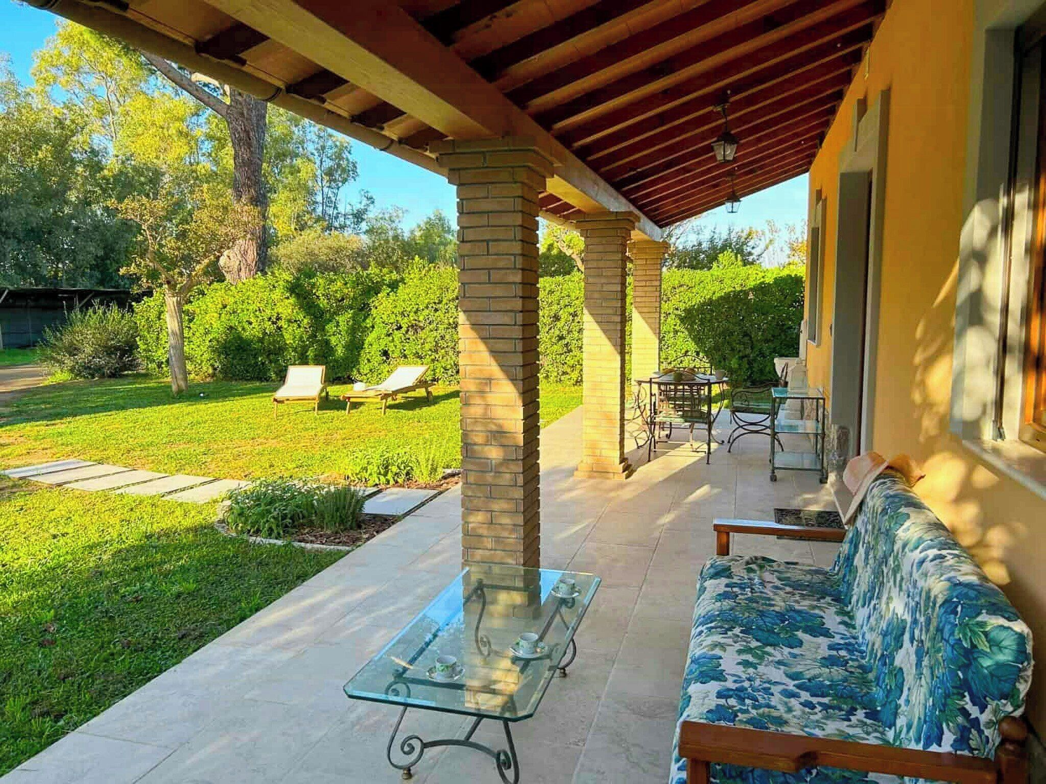 A covered patio area with a glass table, a cushioned bench, and a small table with chairs.