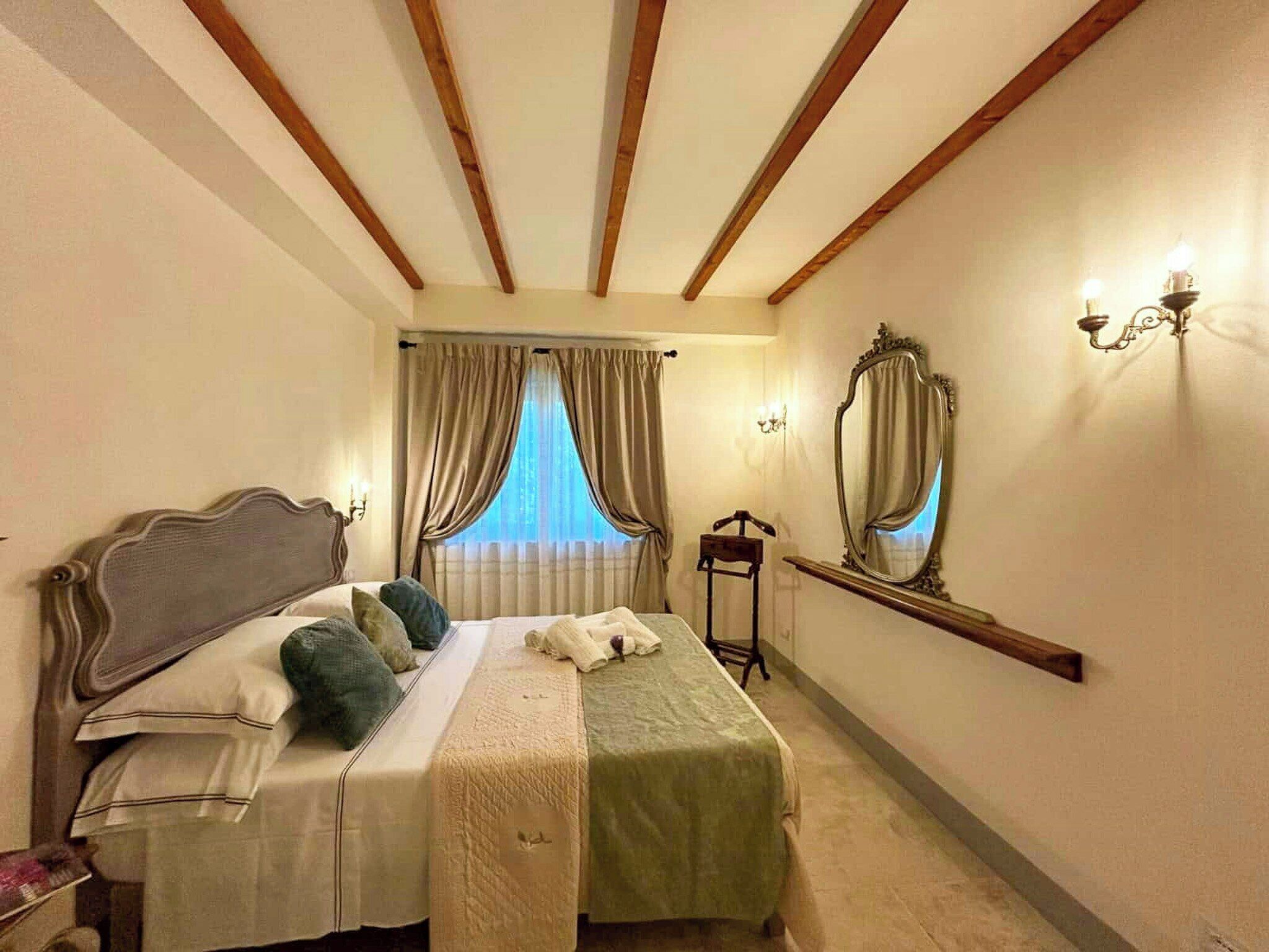 A hotel room with a bed, curtains, a mirror, and a nightstand.