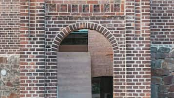 Un edificio de ladrillo con un arco central, dos ventanas encima y una base de piedra.