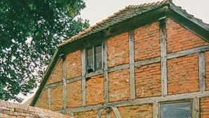 A courtyard with a brick building, green chairs, and a white umbrella. - Apartment in the commandery near the Elbe (Werben)