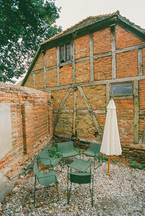 A courtyard with a brick building, green chairs, and a white umbrella. - Apartment in the commandery near the Elbe (Werben)