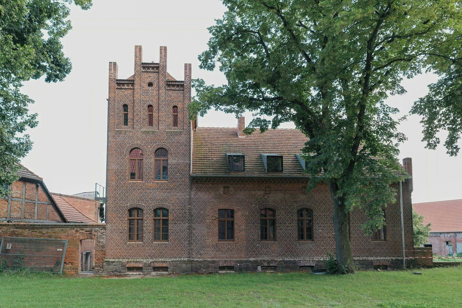 A historic brick building with a prominent tower, large windows, and a surrounding grassy area.