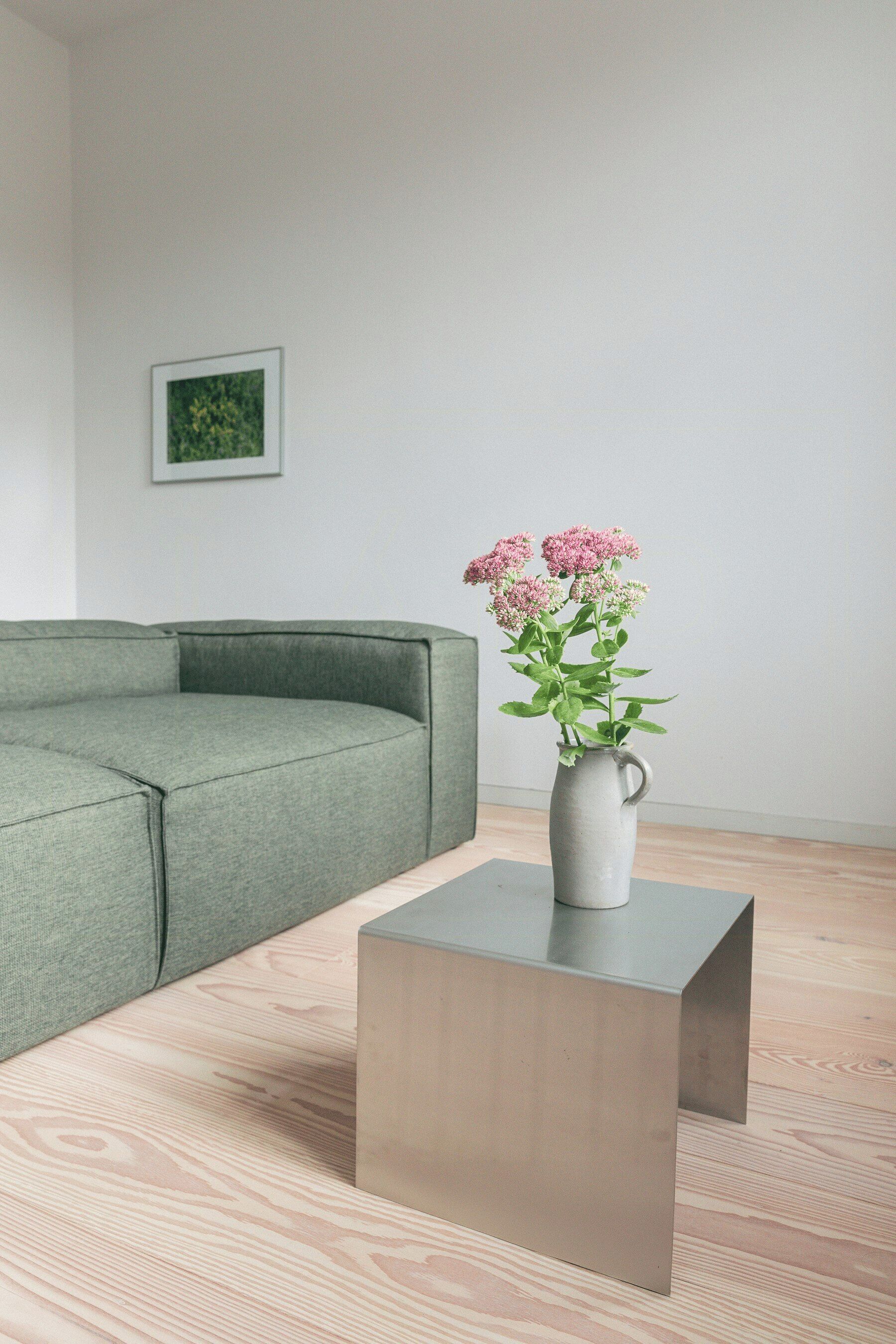 Ein modernes Wohnzimmer mit einer Eckcouch, einem kleinen Tisch und einer Vase mit Blumen.