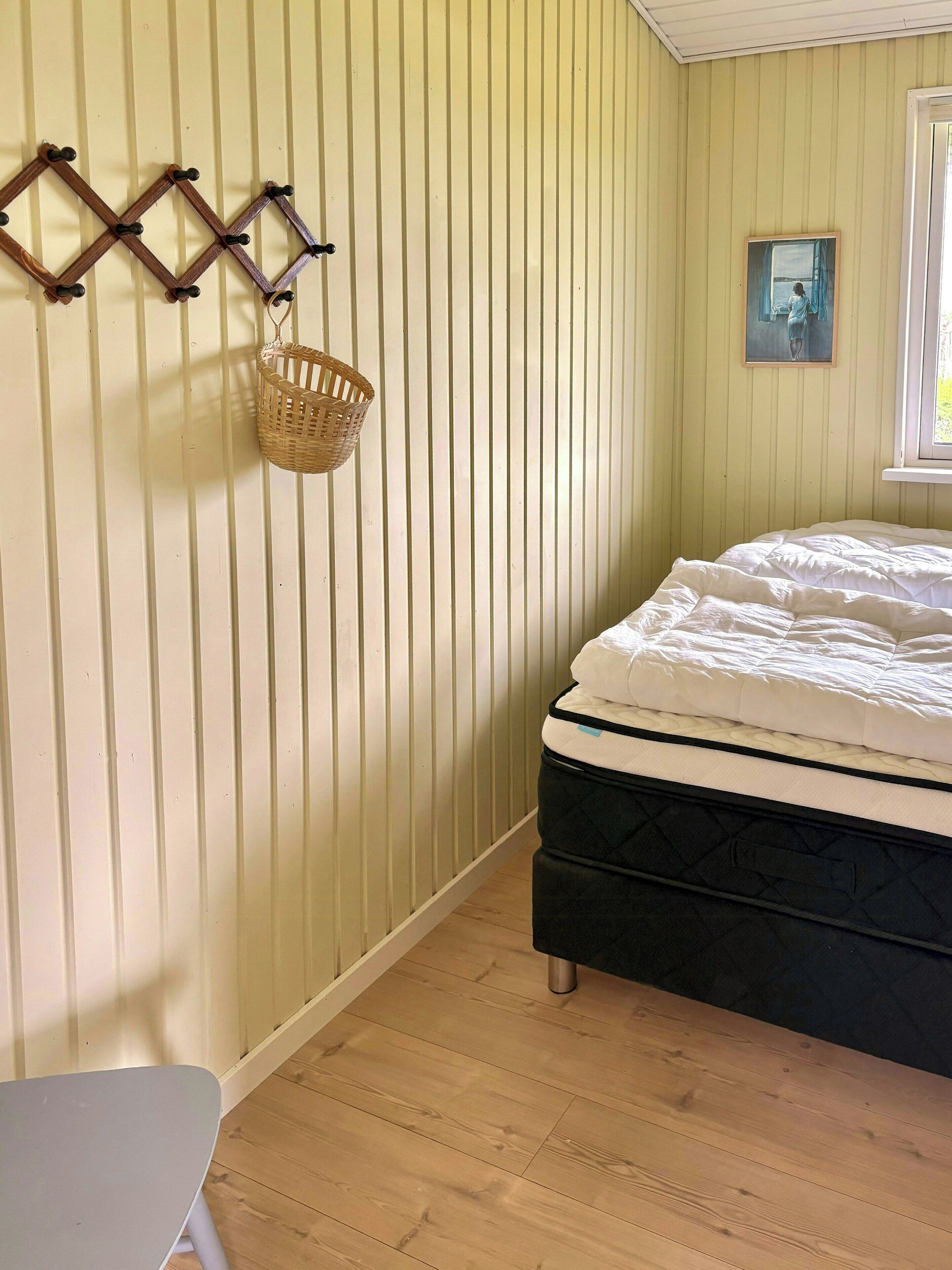 A room with a bed, a wall-mounted basket, and a painting.