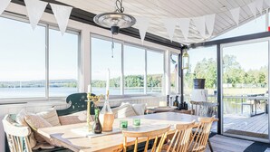 Et træbord med stole, en bænk og udsigt til en sø gennem store vinduer.