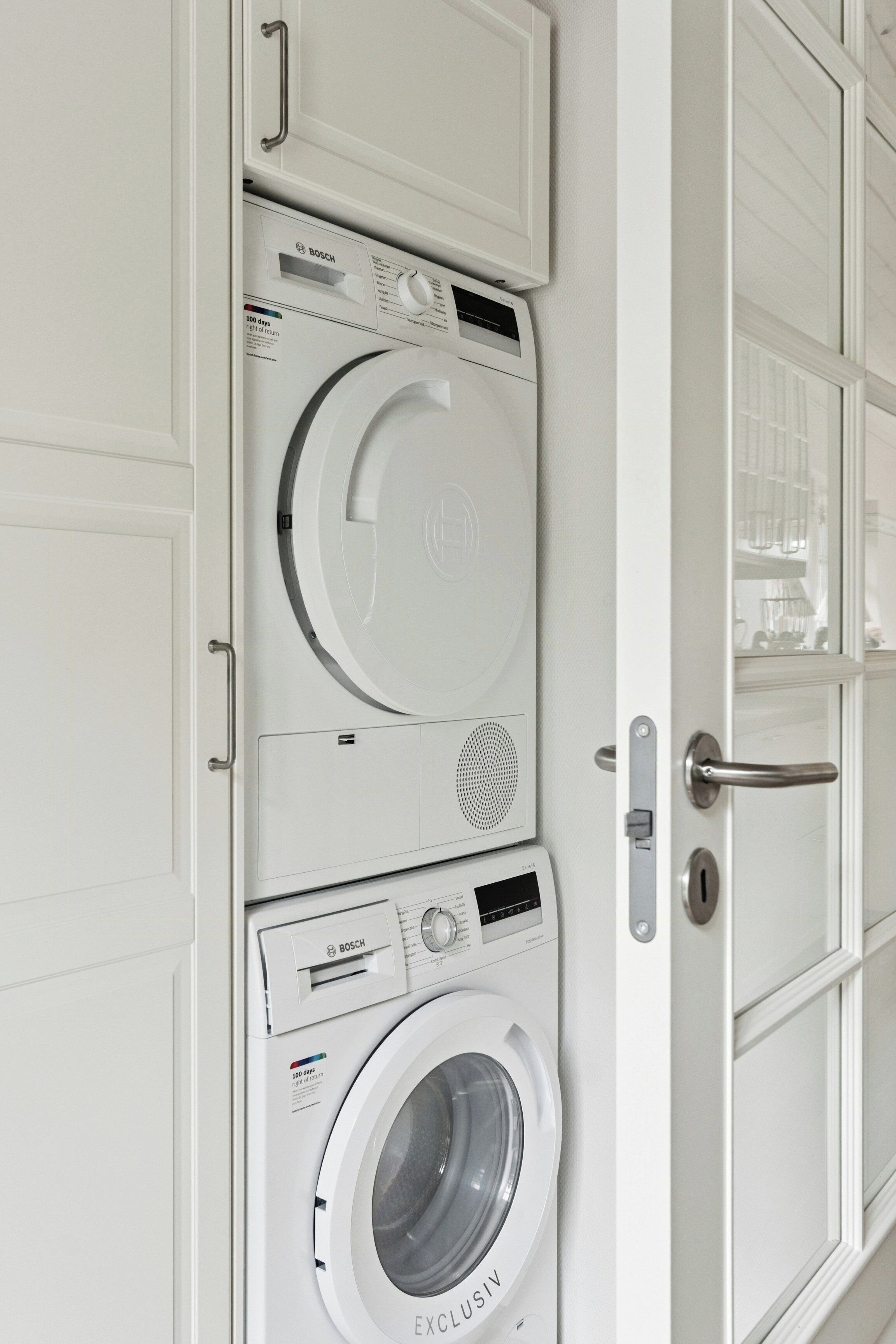 A white laundry room with stacked washing machines and dryers.