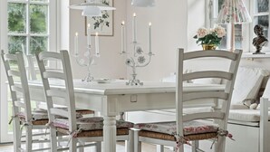 A white dining table with four chairs, candles, and a floral arrangement. - Guest house by lake and forest (Nakskov)