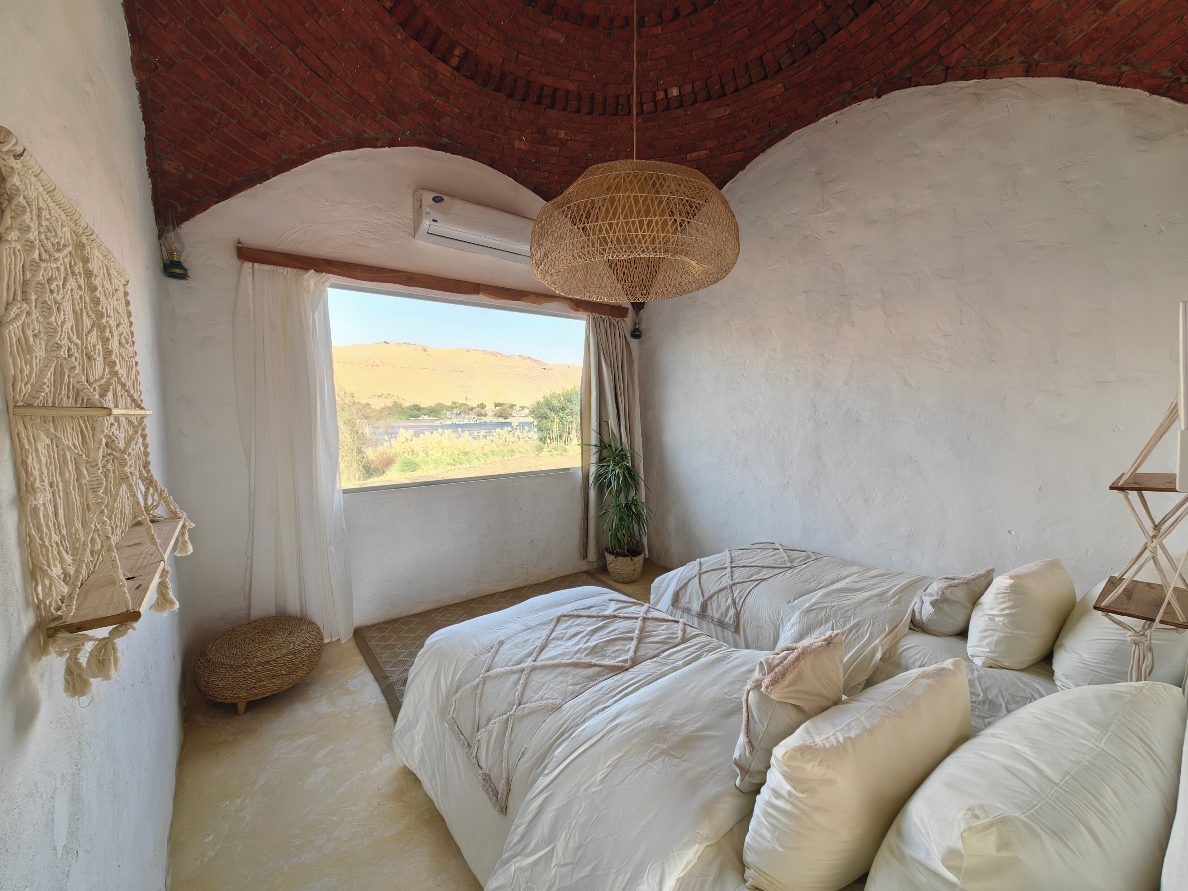 Een slaapkamer met een bed, een hanglamp, een wanddecoratie van macramé en uitzicht op de omgeving.