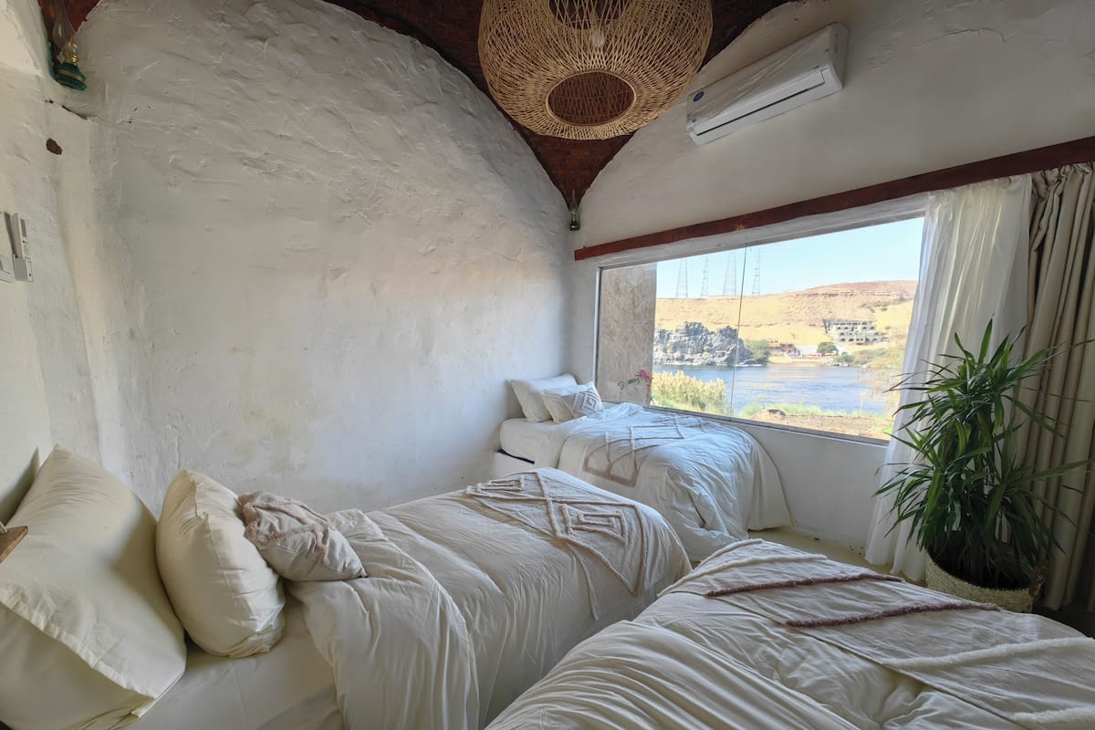 Une chambre avec deux lits, une grande fenêtre donnant sur un paysage, un luminaire suspendu et un appareil de climatisation.