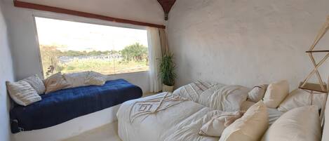 Une chambre avec une grande fenêtre, un lit avec de nombreux oreillers, un luminaire suspendu et un climatiseur fixé au mur.