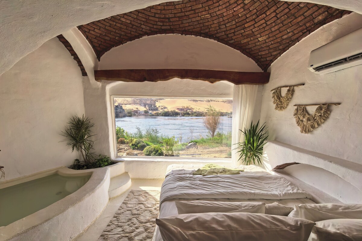 Quarto com vista para um rio, uma banheira e uma cama com almofadas.