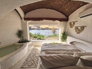 A room with a view of a river, a bathtub, and a bed with pillows. - Nala Narty Nubian house and organic farm (Aswan)