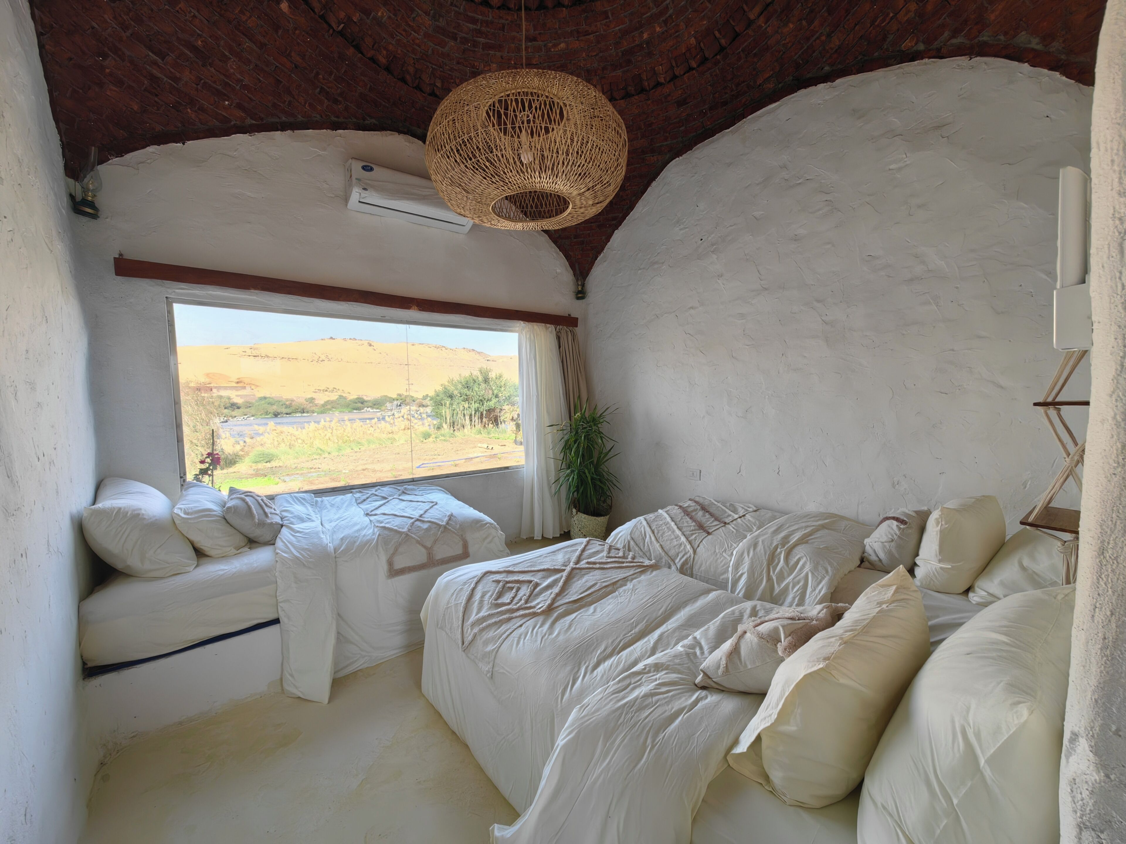 Ein Schlafzimmer mit großem Fenster, einer Hängeleuchte und einem Bett mit vielen Kissen.