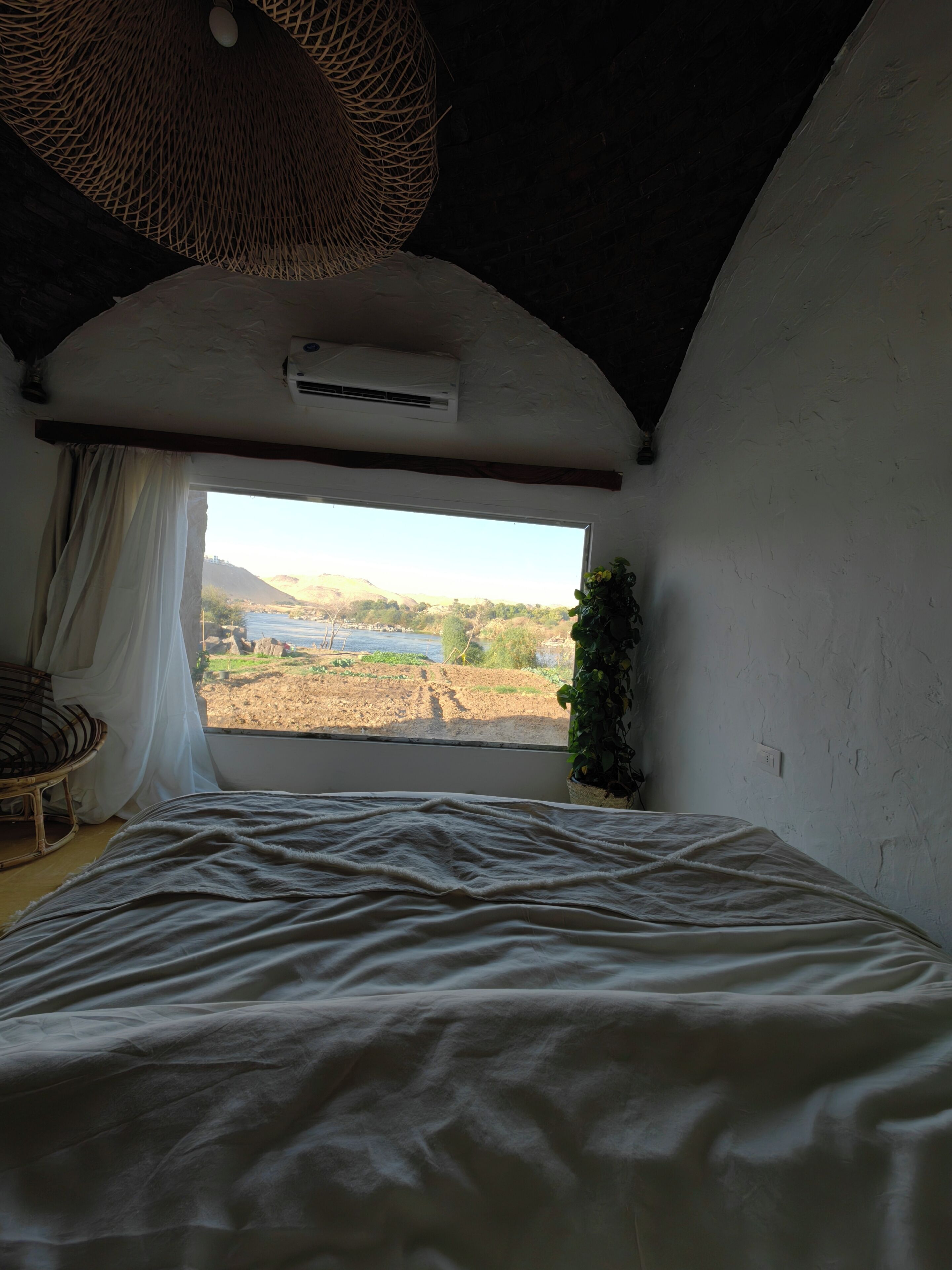 Ein Schlafzimmer mit einem großen Bett, einem Fenster mit Landschaftsblick, einer Pendelleuchte und einer Topfpflanze.