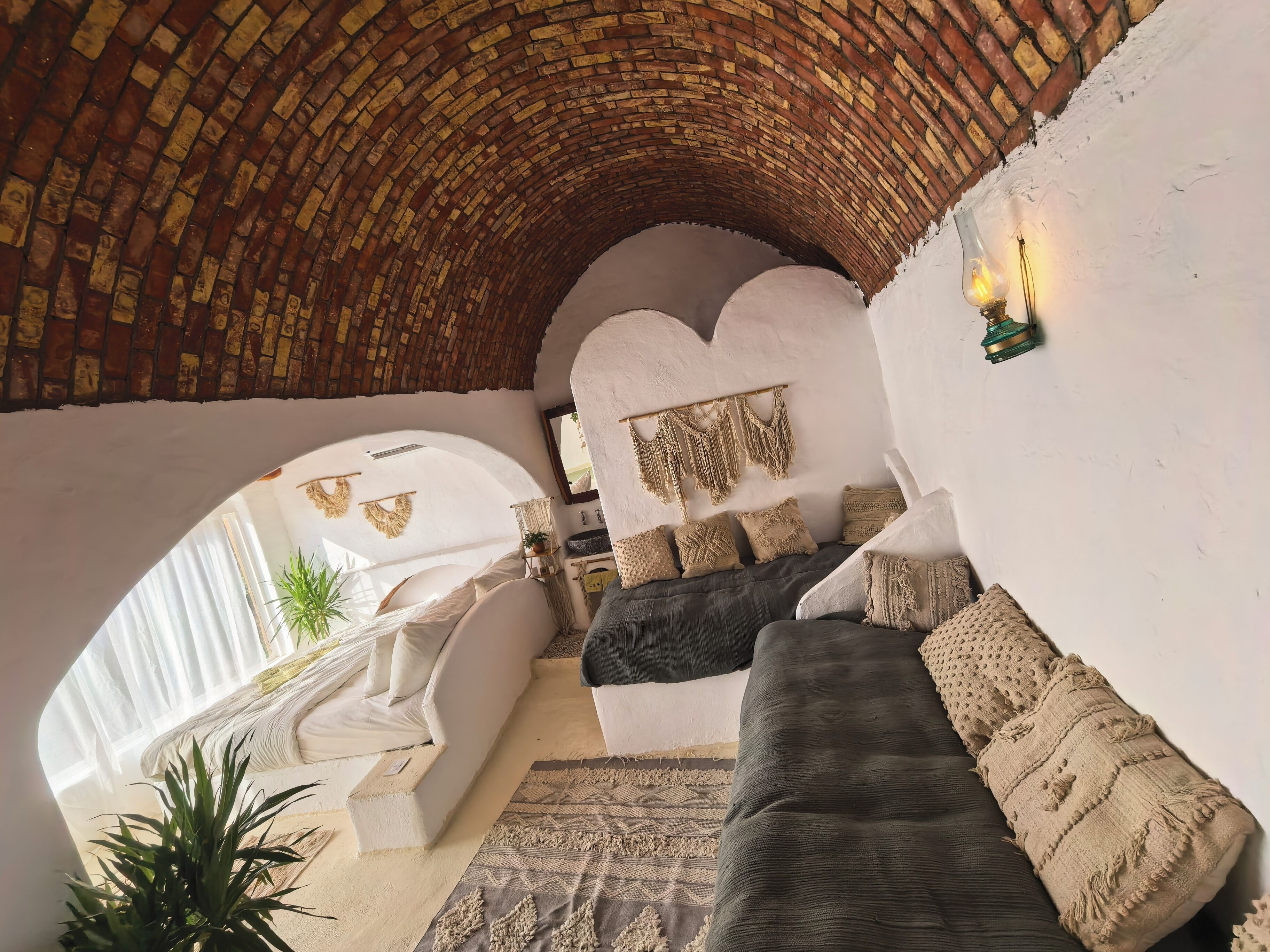 Un salon chaleureux avec un plafond en briques incurvé, un ensemble de canapés, un tapis à motifs et une grande fenêtre.