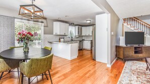 Una cocina moderna con armarios blancos, un comedor con una mesa redonda y sillas, y una escalera que sube a otro nivel.
