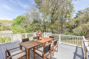 A wooden deck with a table and chairs, surrounded by white railings and trees. - Corn Hill Ranch - East Falmouth (Falmouth)
