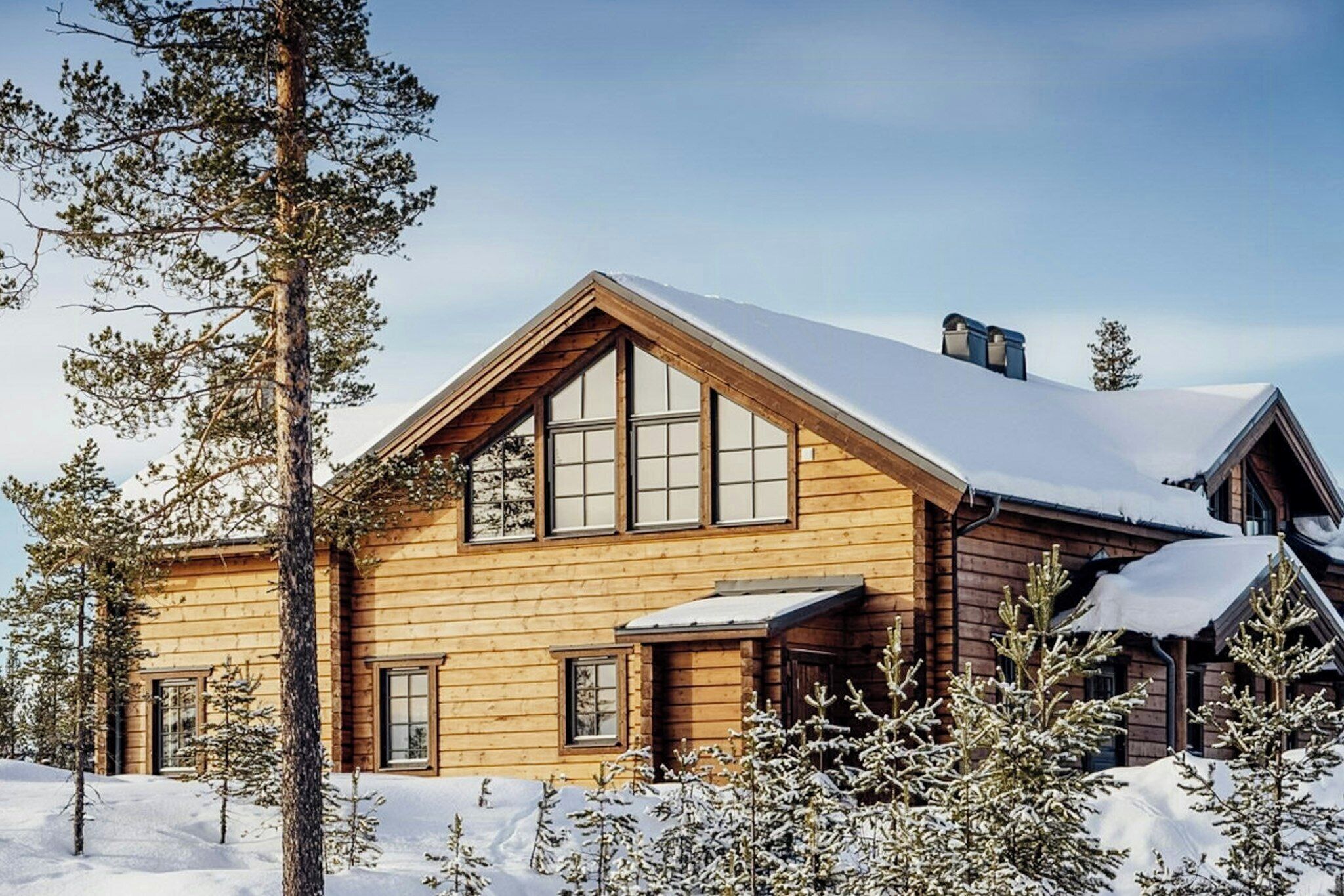 A wooden cabin with a sloped roof, large windows, and a snow-covered landscape.