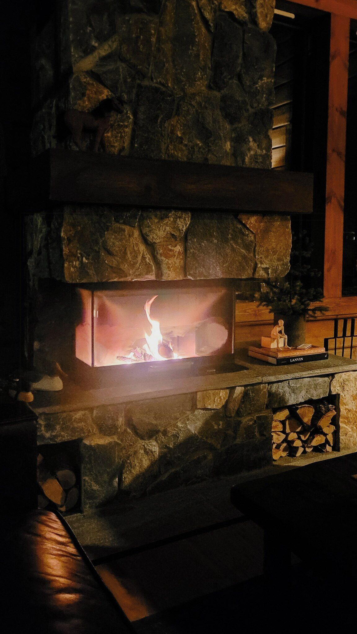 Una chimenea de piedra con fuego, una pequeña estatua y un libro titulado 'LANVIN' en el hogar.