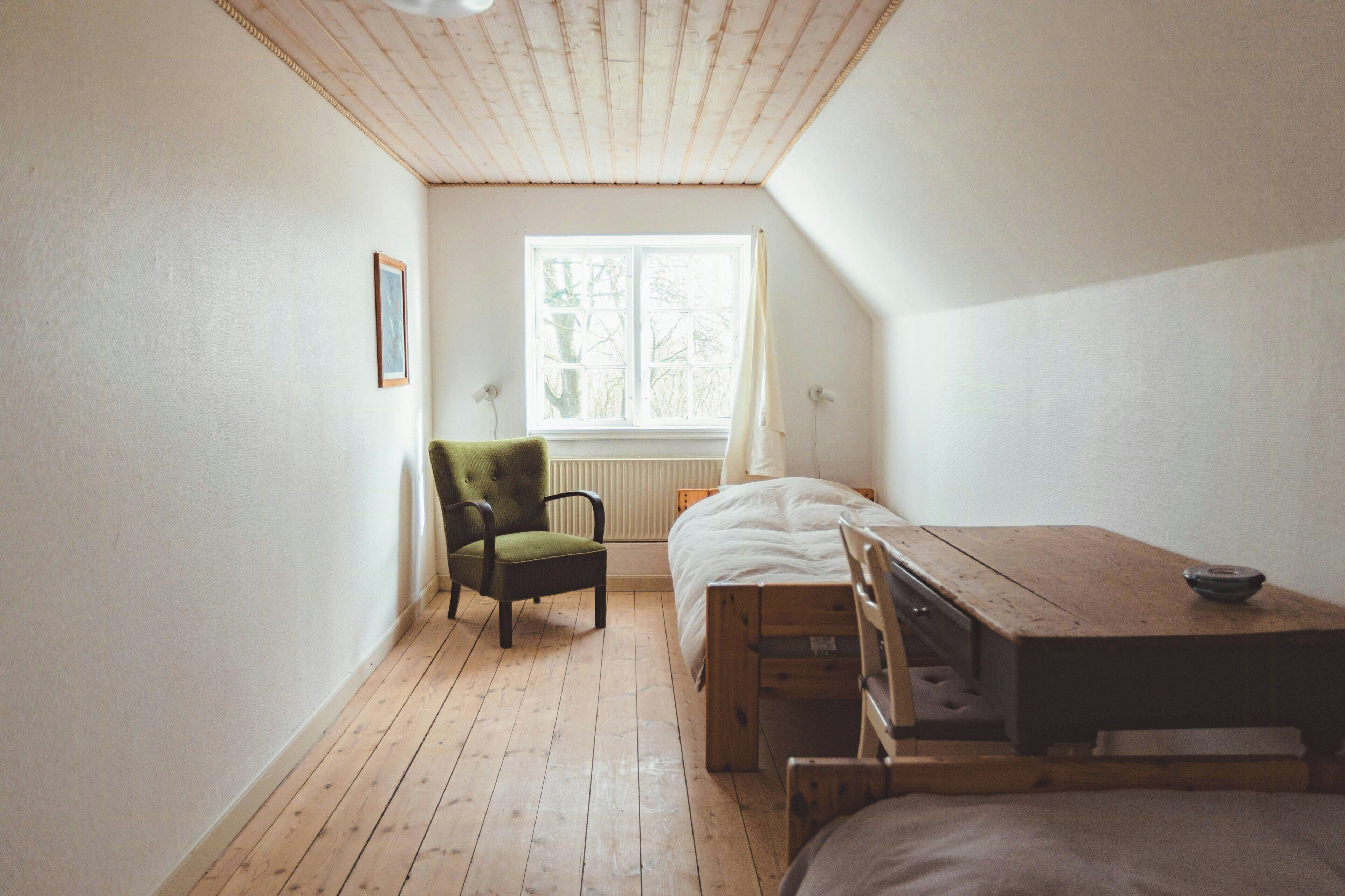 Une pièce avec un plancher en bois, un lit, une chaise, une fenêtre et un radiateur.