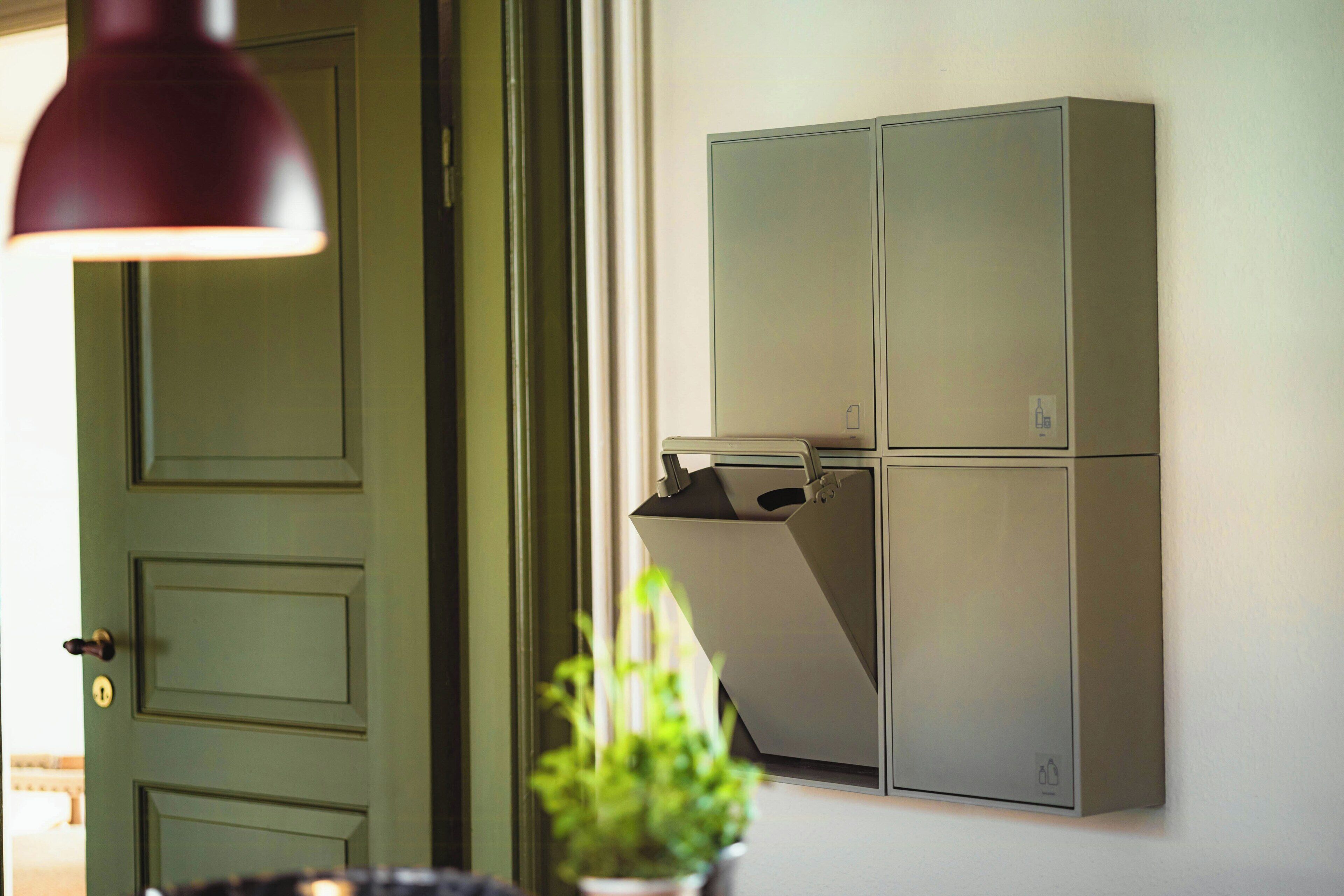 Eine grüne Tür mit Schlüsselloch, ein an der Wand befestigter Schrank mit Ablage und ein Blumentopf.