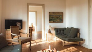 Una sala de estar con sofá, sillón, televisor, lámpara y un cuadro.