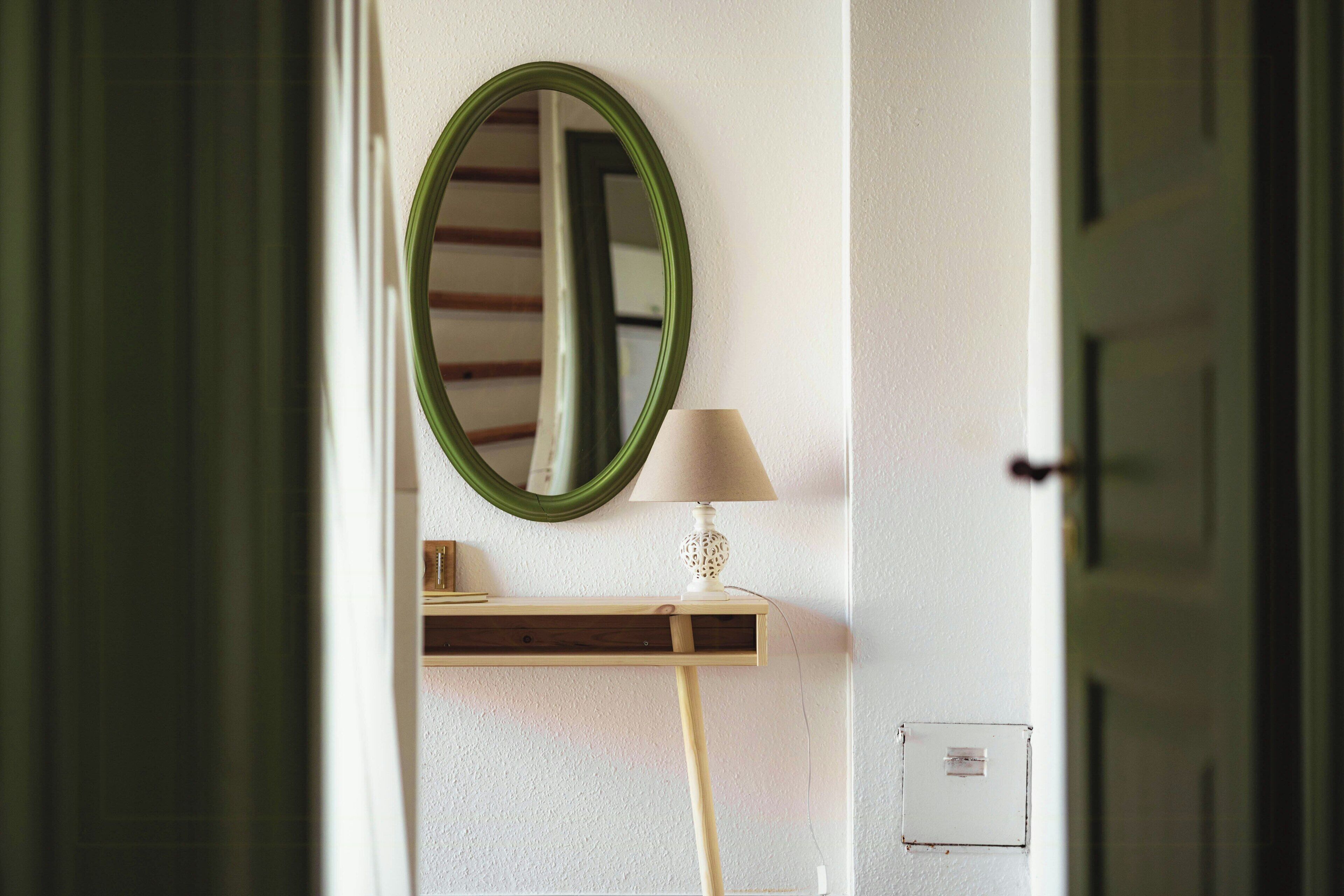 Una habitación con un espejo, una lámpara, un estante de madera y una puerta.
