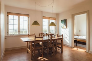 A dining area with a wooden table and chairs, two hanging lamps, and a window with blinds.