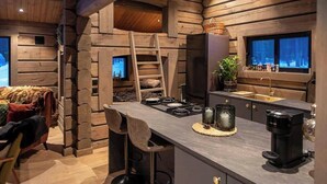 A log cabin interior with a kitchen area, a bar stool, a ladder, and a window with a view. - Cabin with great fishing at Trysilfjellet (Jordet)