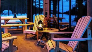 A cozy outdoor seating area with wooden Adirondack chairs, a table with a lantern, and a view of a snowy forest. - Cabin with great fishing at Trysilfjellet (Jordet)