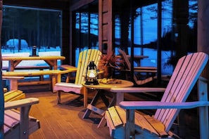 A cozy outdoor seating area with wooden Adirondack chairs, a table with a lantern, and a view of a snowy forest. - Cabin with great fishing at Trysilfjellet (Jordet)