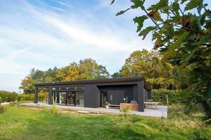 A modern house with a glass facade, a wooden deck, and a small garden area. - Beautiful setting by the sea with light and sky (Grenå)